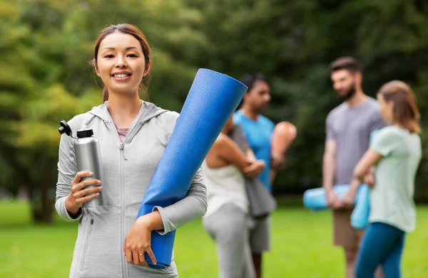 Smiling woman with yoga mat and bottle at park — Stock Photo, Image