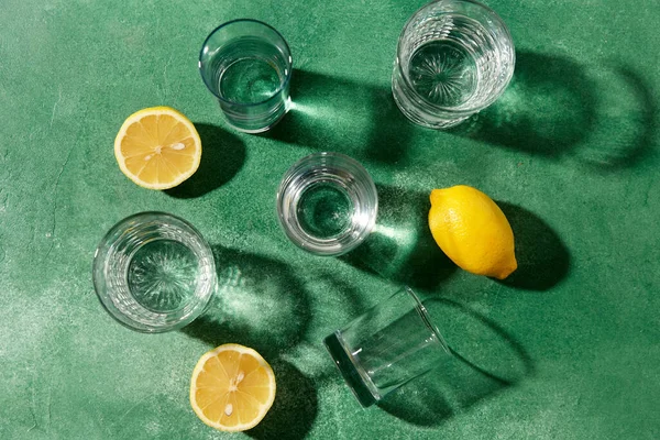 Vasos con agua y limones sobre fondo verde —  Fotos de Stock