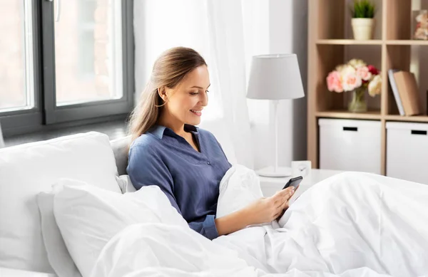 Jeune femme avec smartphone au lit le matin — Photo