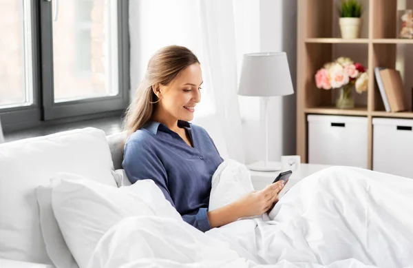 Young woman with smartphone in bed in morning — Stock Photo, Image