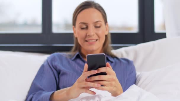 Mujer joven con teléfono inteligente en la cama por la mañana — Vídeos de Stock