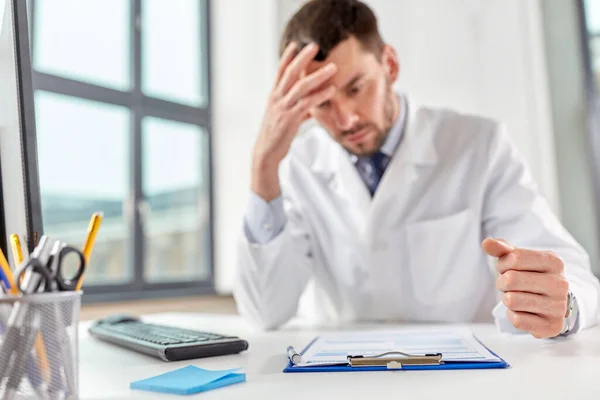 Stressed male doctor with clipboard at hospital — Stock Photo, Image