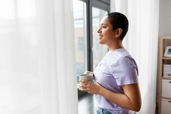 Ευτυχισμένη γυναίκα με καφέ να κοιτάει έξω από το παράθυρο. — Φωτογραφία Αρχείου