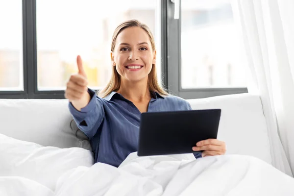 Mujer con tableta pc en la cama mostrando los pulgares hacia arriba —  Fotos de Stock