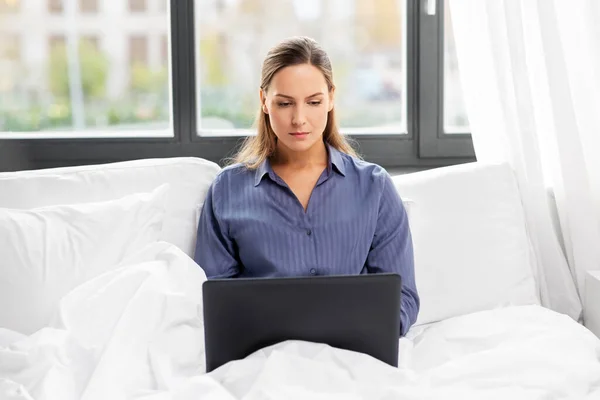 Mujer joven con portátil en la cama en el dormitorio en casa —  Fotos de Stock