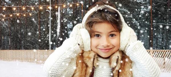 girl in earmuffs at ice skating rink in winter