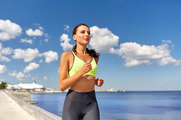 Mujer con auriculares inalámbricos corriendo a la orilla del mar — Foto de Stock