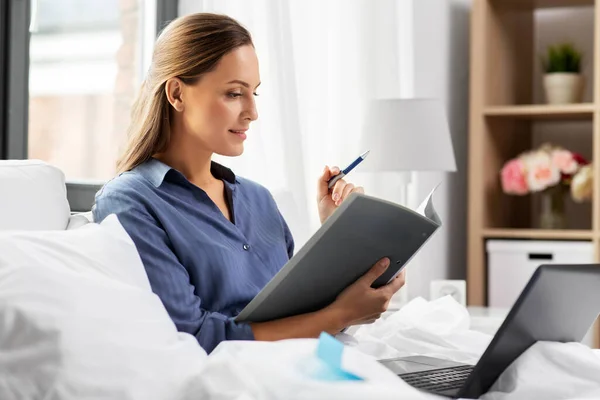 Mujer joven con portátil y papeles en la cama en casa — Foto de Stock