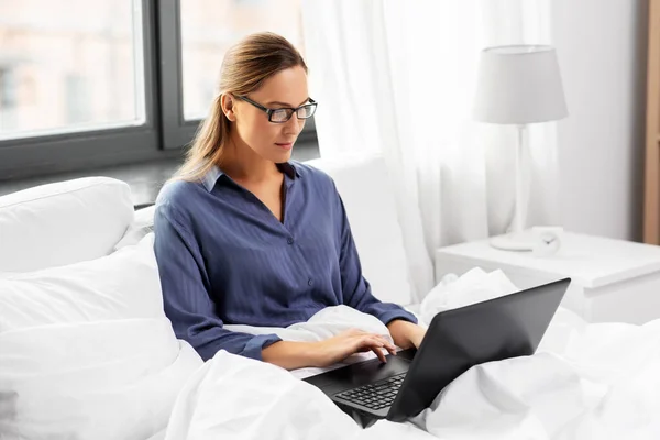 Mujer joven con portátil en la cama en el dormitorio en casa — Foto de Stock