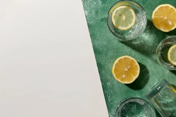 Vasos con agua y limones sobre fondo verde — Foto de Stock