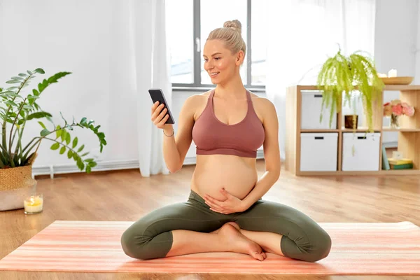 Happy pregnant woman with phone doing yoga at home — Stock Photo, Image