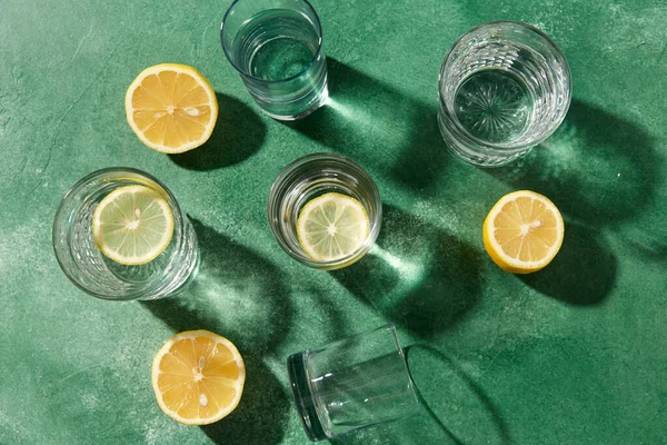 Bicchieri con acqua e limoni su sfondo verde — Foto Stock