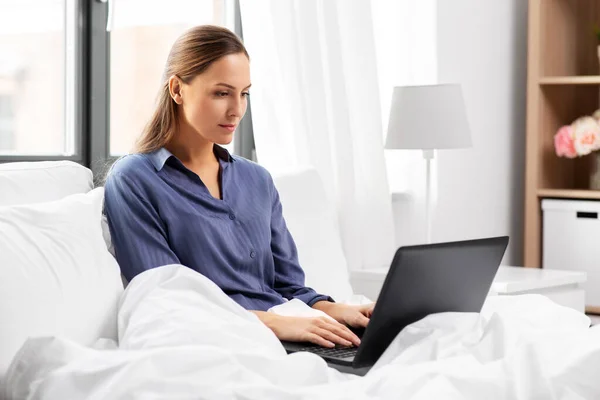 Jeune femme avec ordinateur portable dans le lit à la maison chambre — Photo