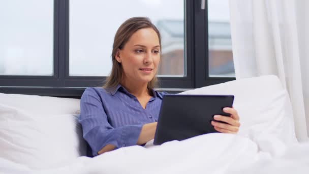 Mujer joven con tableta pc en la cama en el dormitorio en casa — Vídeo de stock