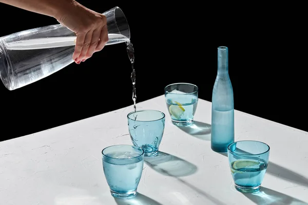 Mano versando acqua ai bicchieri con limone e ghiaccio — Foto Stock