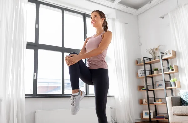 Sonriente joven mujer estirando la pierna en casa — Foto de Stock