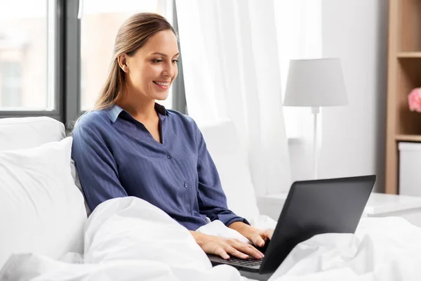 Giovane donna con computer portatile a letto a casa camera da letto — Foto Stock