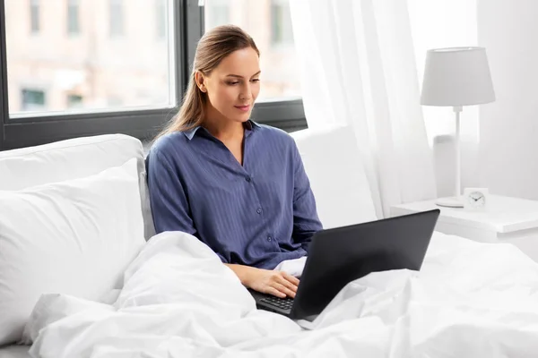 Jeune femme avec ordinateur portable dans le lit à la maison chambre — Photo