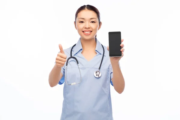 Asiática enfermeira feminina com smartphone mostra polegares para cima — Fotografia de Stock