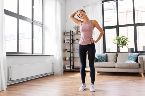 Sonriente joven mujer estirando el cuello en casa — Foto de Stock