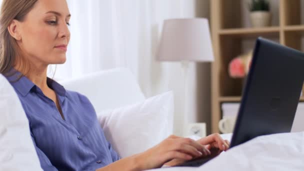 Uśmiechnięta kobieta z laptopem w łóżku w domu sypialnia — Wideo stockowe