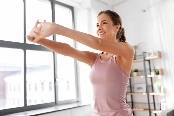 Sonriente joven mujer estirando los brazos en casa — Foto de Stock