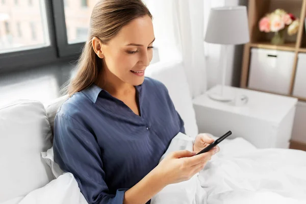 Giovane donna con smartphone a letto al mattino — Foto Stock