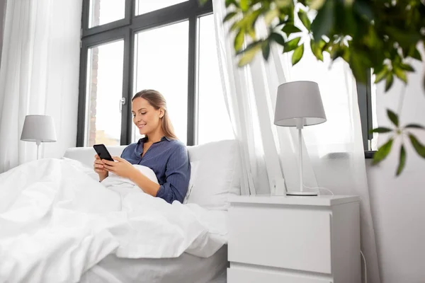 Ung kvinna med smartphone i sängen på morgonen — Stockfoto