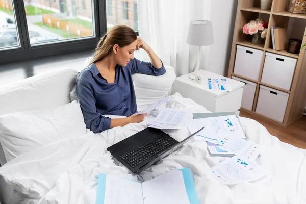 Fiatal nő laptop és papírok az ágyban otthon — Stock Fotó
