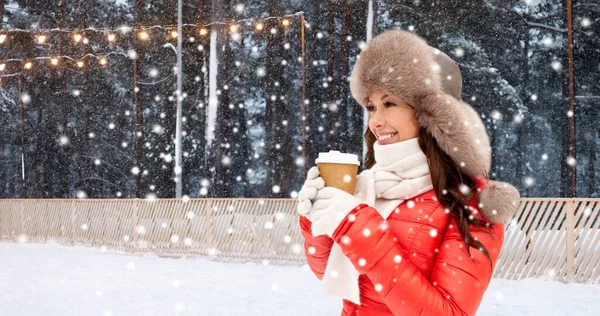 Happy woman with coffee cup over winter ice rink — Stock Photo, Image