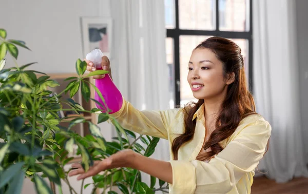 Asiático mujer pulverización houseplant con agua en casa —  Fotos de Stock