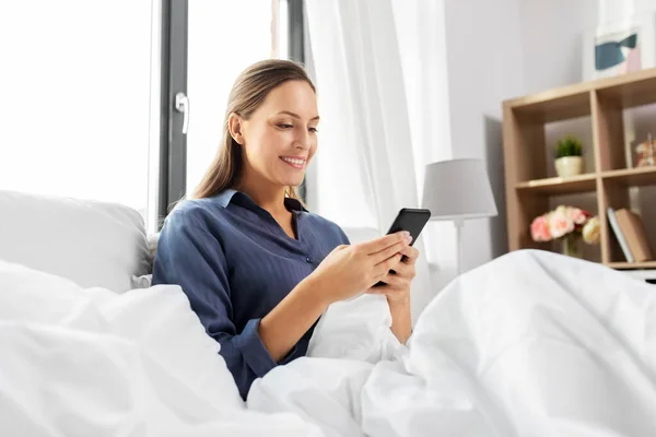 Jonge vrouw met smartphone in bed in de ochtend — Stockfoto