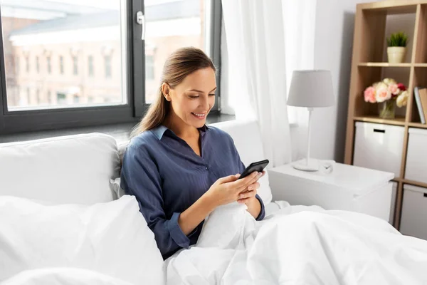 Young woman with smartphone in bed in morning — Stock Photo, Image
