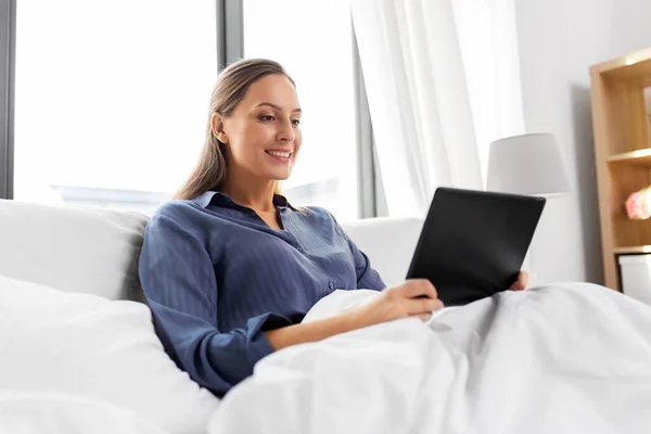 Mujer joven con tableta pc en la cama en el dormitorio en casa —  Fotos de Stock