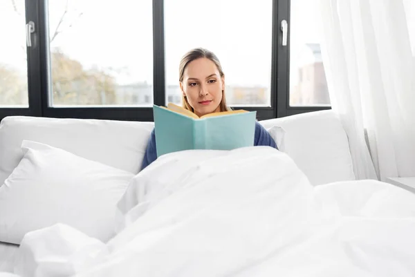 Mujer joven leyendo libro en la cama en casa —  Fotos de Stock