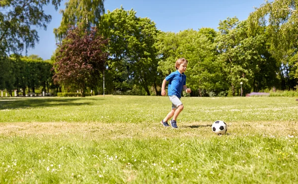 Счастливый мальчик с мячом играет в футбол в парке — стоковое фото