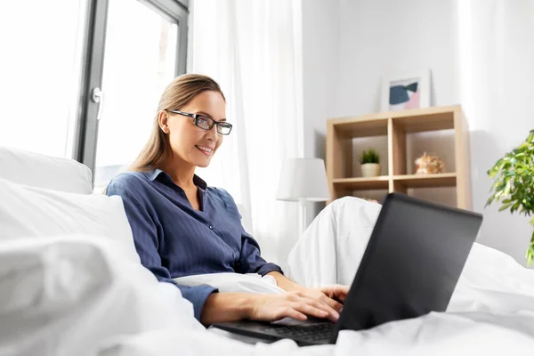 Giovane donna con computer portatile a letto a casa camera da letto — Foto Stock