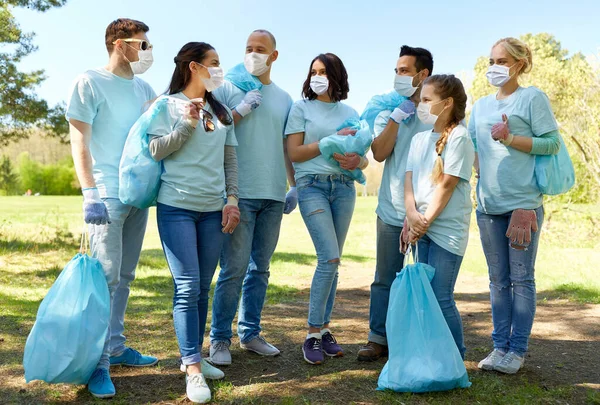 Voluntários em máscaras com sacos de lixo no parque — Fotografia de Stock