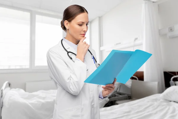 Thinking female doctor with folder at hospital — Stock Photo, Image