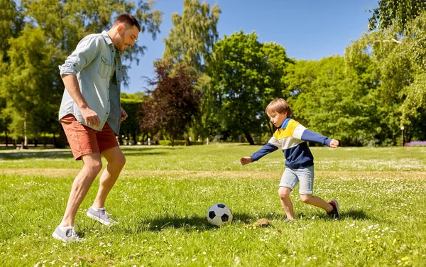 Отец с маленьким сыном играет в футбол в парке — стоковое фото
