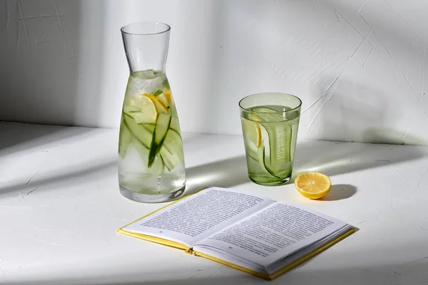 Bicchiere d'acqua con limone e cetriolo e libro — Foto Stock