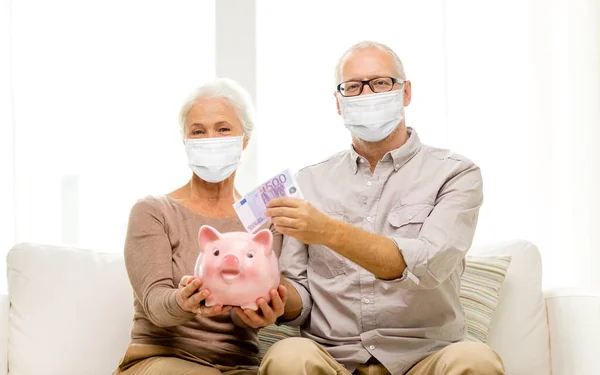 Altes Ehepaar in Masken steckt Geld in Sparschwein — Stockfoto