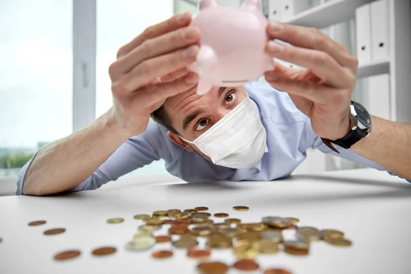 Geschäftsmann in Maske schüttelt Sparschwein um Geld — Stockfoto