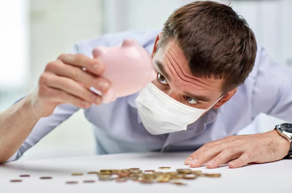 Businessman in mask shaking piggy bank for money — Stok fotoğraf