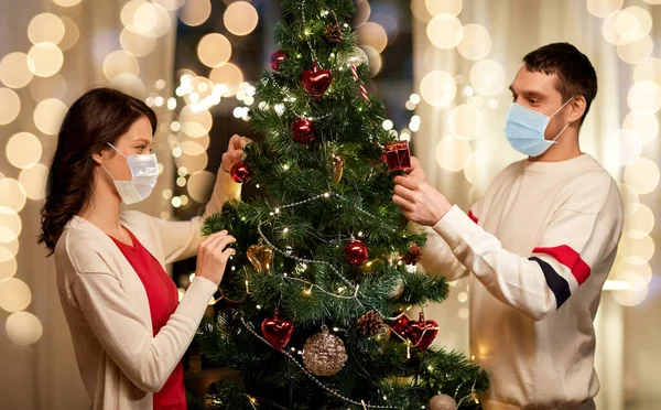 Couple in masks decorating christmas tree at home — Stock Photo, Image