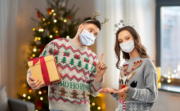 Couple in masks, christmas sweaters with gifts — Stock Photo, Image