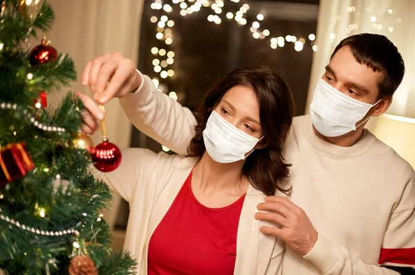 Couple in masks decorating christmas tree at home — Stock Photo, Image