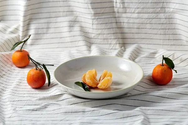 Натюрморт с мандаринами на тарелке над драпировкой — стоковое фото