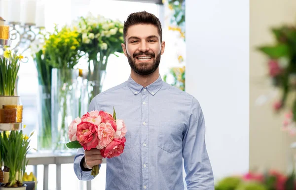 Szczęśliwy uśmiechnięty mężczyzna z piwoniami w kwiaciarni — Zdjęcie stockowe