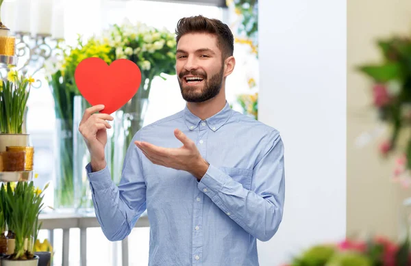 Smiling young man with red heart at flower shop — Stock Photo, Image